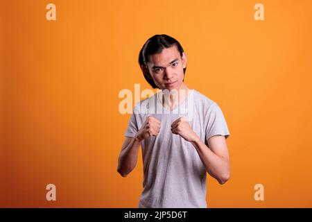 Ernst starken jungen asiatischen Mann in Kampfpose, Stärke Konzept stehen. Wütender Teenager in Boxposition mit geballten Fäusten Porträt, aggressive Kämpfer Blick auf die Kamera Stockfoto