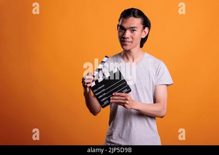 Junger asiatischer Kameramann Assistent schlappt Film machen Klapperbrett, Filmszenen schießen. Kinematographie, Videoproduktion, lächelndes Klapper-Lader-Portrait, Filmemacher mit Schiefer Stockfoto