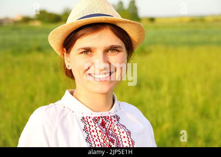 Unschärfe junge ukrainische Frau Porträt. Wiese Natur Hintergrund. Junge ukrainer. Lächelndes ukrainisches Mädchen zeigt Geste Liebe. Wyschywanka Stockfoto