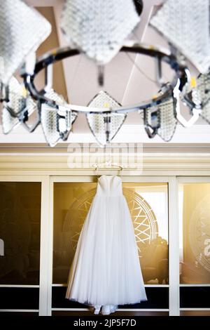 Hochzeitskleid hängt an der Wand unter dem Kronleuchter. Stockfoto