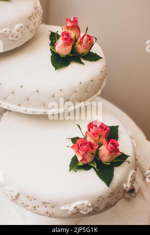 Mehrstufiger Hochzeitstorte auf dem mit Rosen geschmückten Tisch. Stockfoto