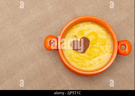 Hausgemachter süßer Maispudding in Brasilien als Curau oder Canjica Nordestina in Keramikschale bekannt. Zimtpulver in Herzform. Stockfoto