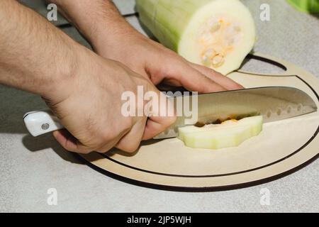 Rezept für Zucchini-Krapfen. Schritt 2 - Zucchini schneiden. Hände schneiden grüne Zucchini in Würfel. Kochen veganer Gemüsepfannkuchen. Stockfoto