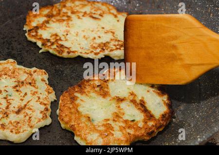 Rezept für Zucchini-Krapfen. Schritt 5 - Pfannkuchen in der Pfanne goldbraun braten. Pfannkuchen mit Holzspachtel umschlagen. Stockfoto