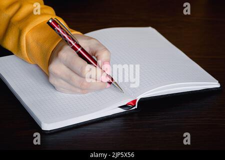 Frau schreibt in leerem Notizbuch. Nahaufnahme des Hand-Haltestifts. Geschäftsfrau macht sich im Büro Notizen. Stockfoto