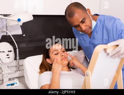 Männliche Kosmetikerin, die Frau vor der Gesichtsbehandlung konsultiert Stockfoto