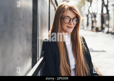 Porträt einer erfolgreichen Frau, die lächelnd und mit einer Brille direkt in die Kamera schaut. Schönes Mädchen Porträt. Lifestyle in der Stadt. Reisemode Stockfoto