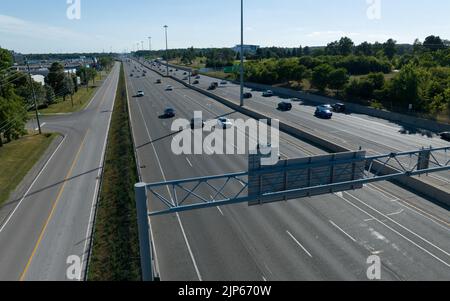 Ein Luftbild über einer großen, mehrspurigen Autobahn, während der Verkehr an einem klaren, sonnigen Tag unter einem Überführung-Schild vorbeifährt. Stockfoto
