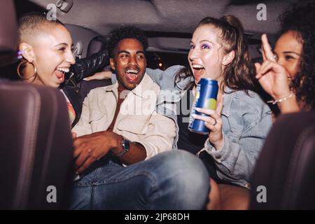 Fröhliche Freunde, die sich auf dem Rücksitz eines Autos amüsieren. Eine Gruppe verschiedener junger Menschen, die zusammen lachen, während sie in einem Taxi sitzen. Vier glückliche Freunde havi Stockfoto