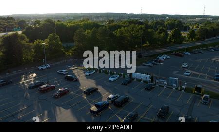 Eine Luftaufnahme mit Blick auf eine Tesla Supercharger-Station auf einem Parkplatz, während der Abend im Hintergrund durchscheint. Stockfoto