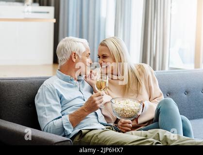 Erste Regel einer glücklichen Ehe Date einander. Ein glückliches reifes Paar entspannen zusammen mit Wein und Popcorn auf dem Sofa zu Hause. Stockfoto