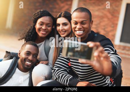 Gather round, seine Selfie-Zeit. Eine Gruppe von Studenten, die zusammen Selfies auf dem Campus machen. Stockfoto