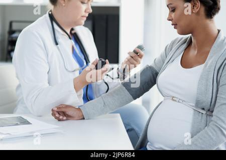 Alles scheint normal zu sein. Eine selbstbewusste Ärztin, die tagsüber den Blutdruck einer Schwangeren in einem Krankenhaus überprüft. Stockfoto