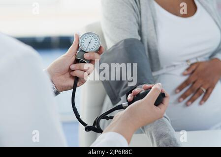 Eine nicht erkennbare Ärztin, die den Blutdruck einer Schwangeren im Laufe des Tages in einem Krankenhaus überprüft. Stockfoto