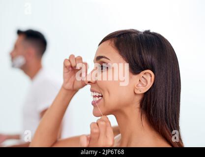 Erfrischend für einen schönen Tag. Eine attraktive junge Frau, die ihre Zähne im Badezimmer mit Zahnseide ausgab. Stockfoto