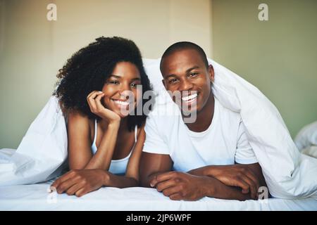 Liebe beginnt den Tag mit einem Lächeln. Porträt eines glücklichen jungen Paares, das sich unter einer Bettdecke im Schlafzimmer entspannt. Stockfoto
