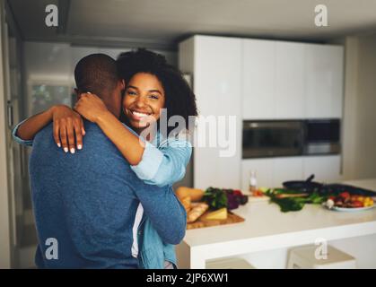 Ich liebe es, dich zu haben. Porträt eines fröhlichen jungen Paares, das sich gegenseitig hält und tagsüber einen zarten Moment in der Küche zu Hause teilt. Stockfoto