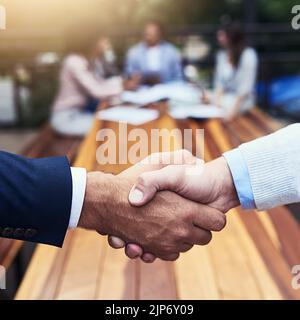 Und der Deal wurde besiegelt. Nahaufnahme von zwei nicht erkennbaren Geschäftsleuten, die sich im Hintergrund mit ihren Kollegen die Hände schüttelten. Stockfoto