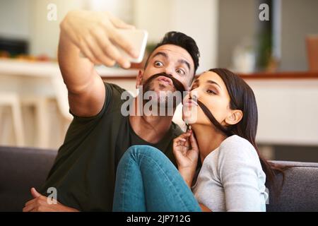 Sie teilen viele unbeschwerte Momente miteinander. Ein junges Paar, das zu Hause Selfies macht. Stockfoto