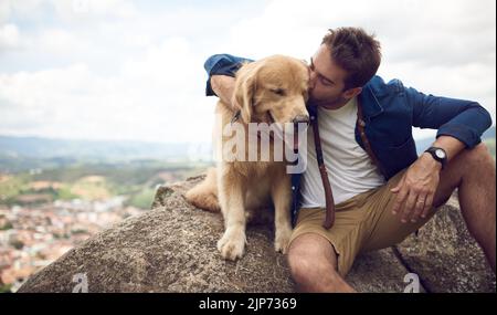 Ich bin dankbar für meinen Hund jeden Tag. Ein hübscher junger Mann, der nach einem Tag auf einem Felsen mit seinem goldenen Retriever sitzt. Stockfoto