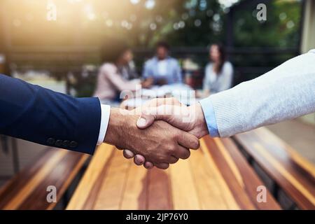 Neue Fusionen sind für das Geschäft von großer großer Geschäftig. Nahaufnahme von zwei nicht erkennbaren Geschäftsleuten, die sich im Hintergrund mit ihren Kollegen die Hände schüttelten. Stockfoto