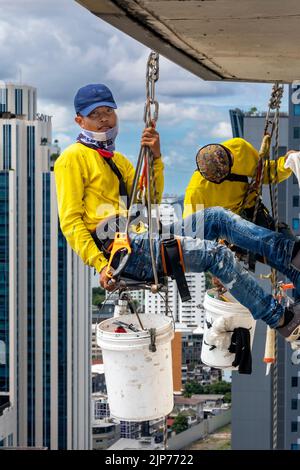 Thailändische Arbeiter reparieren die Fenster des Hochhauses über Bangkok, Thailand Stockfoto