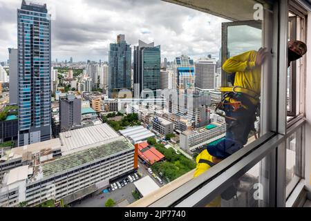 Thailändische Arbeiter reparieren die Fenster des Hochhauses über Bangkok, Thailand Stockfoto