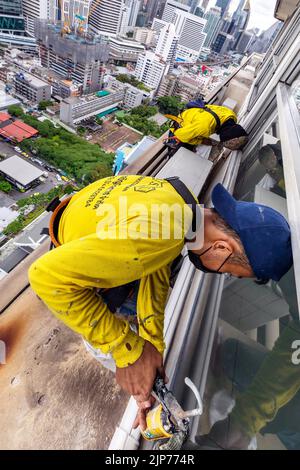 Thailändische Arbeiter reparieren die Fenster des Hochhauses über Bangkok, Thailand Stockfoto