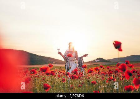 Eine Frau, die bei Sonnenuntergang Erdbeeren auf einem Mohnfeld isst. Vorderansicht. Stockfoto