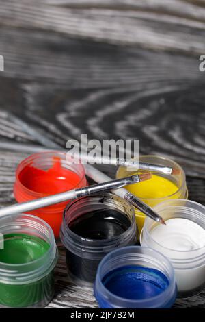 Ein Set aus Gouache und Bürsten. Farbdosen öffnen. Auf Kiefernbrettern. Nahaufnahme. Stockfoto