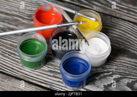 Ein Set aus Gouache und Bürsten. Farbdosen öffnen. Auf Kiefernbrettern. Nahaufnahme. Stockfoto