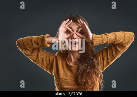 Dumm zu sein. Studioporträt einer fröhlichen jungen Frau, die mit ihren Händen ein Gesicht macht, während sie vor einem dunklen Hintergrund steht. Stockfoto