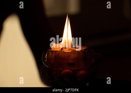 Die Hand einer Frau hält eine brennende Kerze im Dunkeln, Kerzenflamme und Religion, Gebet und Kerze Stockfoto