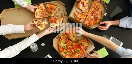 Junge Leute essen leckere Pizza am Tisch im Büro, Draufsicht Stockfoto