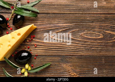 Komposition mit leckeren schwarzen Oliven, Käse und Pfefferkörnern auf Holzhintergrund Stockfoto