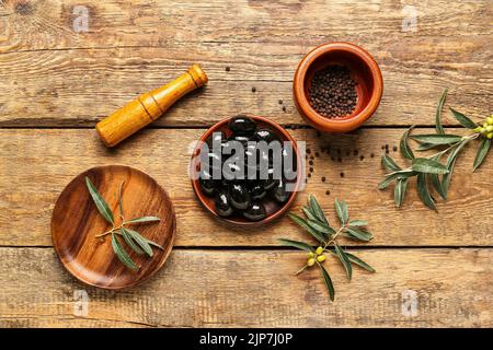 Komposition mit leckeren schwarzen Oliven, Pfefferkörnern und Mörtel auf Holzgrund Stockfoto