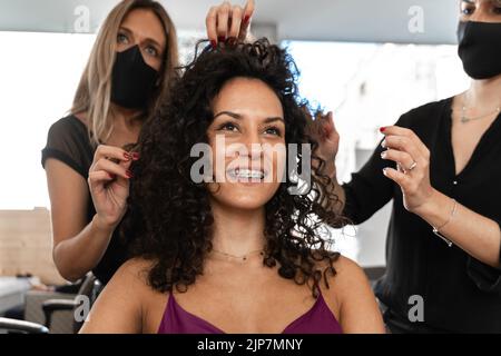 Portrait von zwei Friseuren mit Maske, die an einem Kunden in einem Salon arbeiten Stockfoto