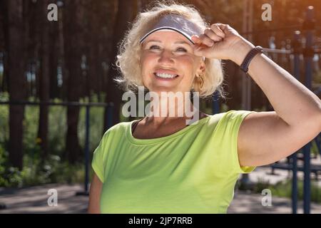 Reife Frau in weißer Mütze sieht die Sonne lächelnd aus der Nähe Stockfoto