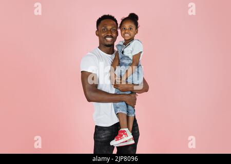 Glücklicher afroamerikanischer Mann, der kleine lächelnde Tochter über rosa Studiohintergrund hält, Panorama mit freiem Kopierraum, Banner Stockfoto