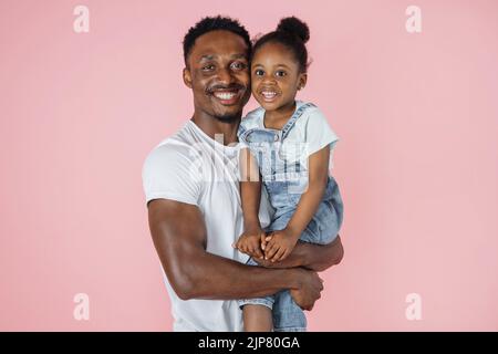 Vater- und Tochterverbindung. Close uo Porträt von positiven afrikanischen Mann und kleines Mädchen berühren Köpfe, Kuscheln auf rosa Studio-Hintergrund. Stockfoto