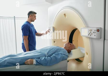 Der MTRA, der den Computertomographie-Scanner verwendet, um einen liegenden Patienten in der Radiologieabteilung des Krankenhauses zu scannen. CT-Scanner Stockfoto