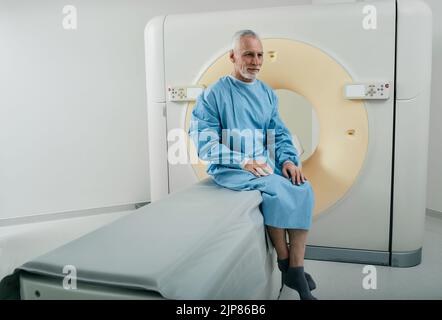 Alter Mann mit CT-Scan-Verfahren sitzt auf CT-Maschinenscanner in der Radiologie Abteilung des Krankenhauses Stockfoto