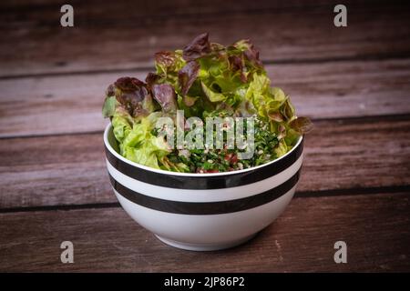 Petersiliensalat oder Tabbouleh, einfaches und gesundes klassisches vegetarisches Gericht mit Bulgur, Tomaten, Petersilie, Frühlingszwiebeln und Minze, Olivenöl auf dunklem Holz Stockfoto