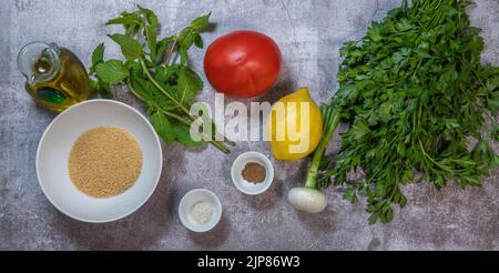 Zutaten für einen Petersiliensalat oder Tabbouleh, einfaches und gesundes, klassisches vegetarisches Gericht mit Bulgur, Tomaten, Petersilie, Frühlingszwiebeln und Minze, Oliven Stockfoto