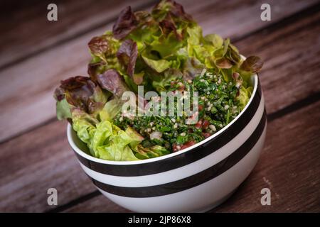 Petersiliensalat oder Tabbouleh, einfaches und gesundes klassisches vegetarisches Gericht mit Bulgur, Tomaten, Petersilie, Frühlingszwiebeln und Minze, Olivenöl auf dunklem Holz Stockfoto