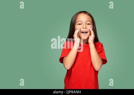 Porträt eines kleinen hübschen Mädchens, das seitlich steht und jemanden anruft, der ihre Hand in der Nähe ihres Mundes hält Stockfoto