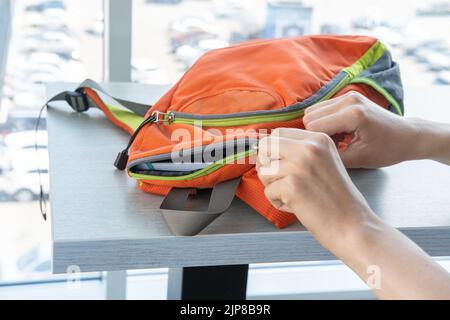 Damenhänden ziehen einen orangen Schulrucksack mit Schulbedarf, Büchern, Büro und Laptop auf den Tisch. Zurück zum Schulkonzept. Stockfoto