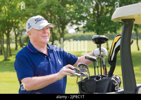 Eine flache Aufnahme eines alten Mannes, der eine Baseballmütze trägt und Golfschläger aus einer Golftasche auswählt Stockfoto