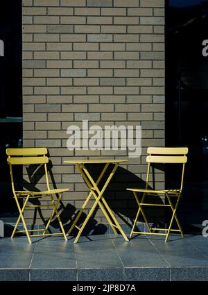 Elegante gelbe Tische und Stühle des Café im Freien an einer Ziegelwand Stockfoto