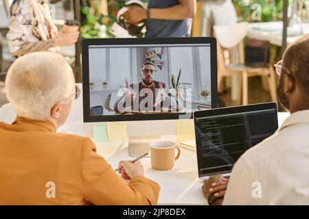 Rückansicht von Geschäftsleuten, die mit ihrem Kollegen im Büro Videoanruf am Computer führen Stockfoto
